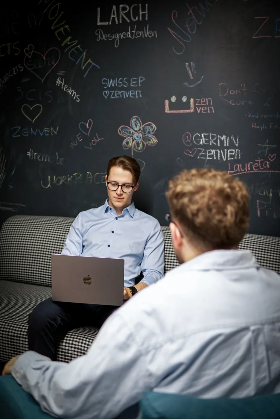 Two twinalps engineers working together on a studio couch under a chalkboard wall